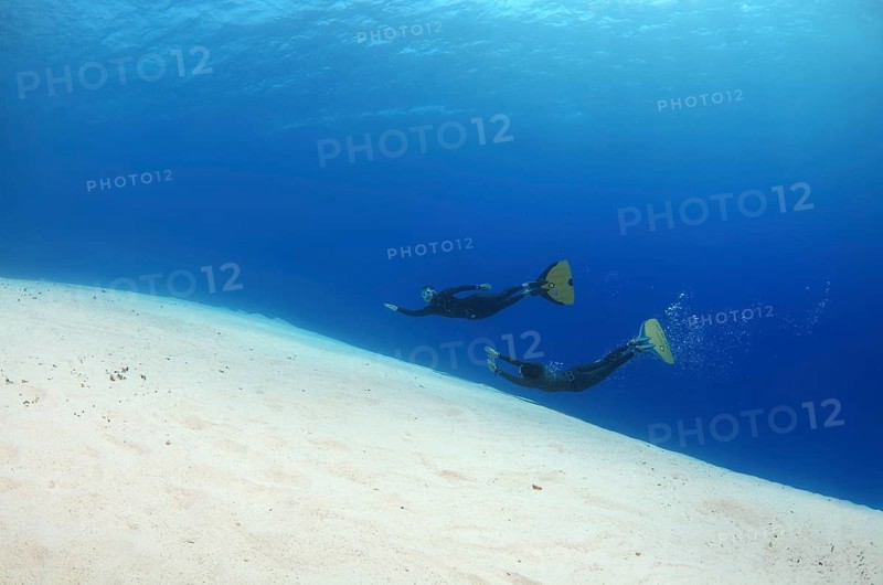 Freediver swimming over a sandy ocean bottom