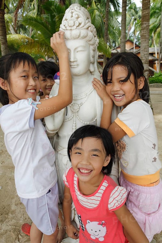 Chinese girls laughing by a Buddha statue on the beach by Dongjiao Yelin
