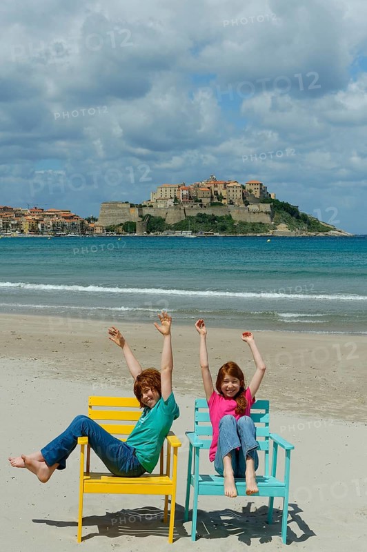 Children sitting in colorful beach chairs on the beach of Calvi