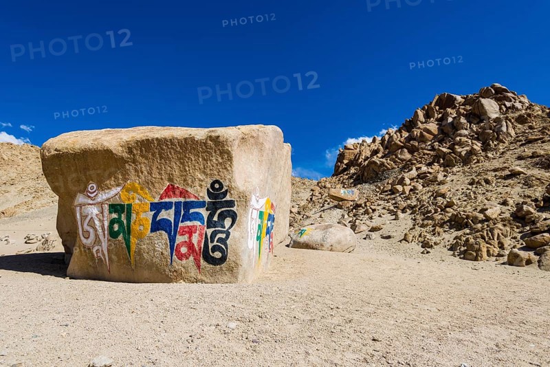 A big Tibetan Mani Stone with the Mantra "Om Mani Padme Hum" colorfully engraved on a hill above the Indus Valley