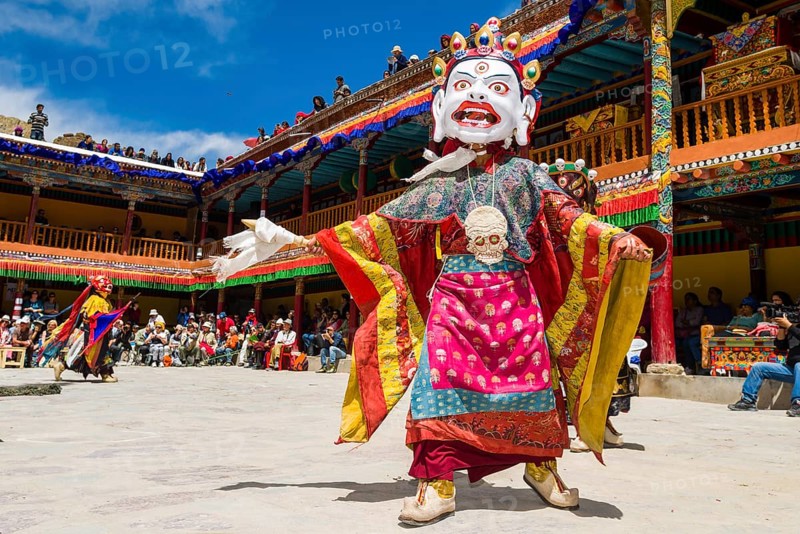 Monks with big wooden masks and colorful costumes are performing ritual dances at Hemis Festival in the courtyard of the monastery