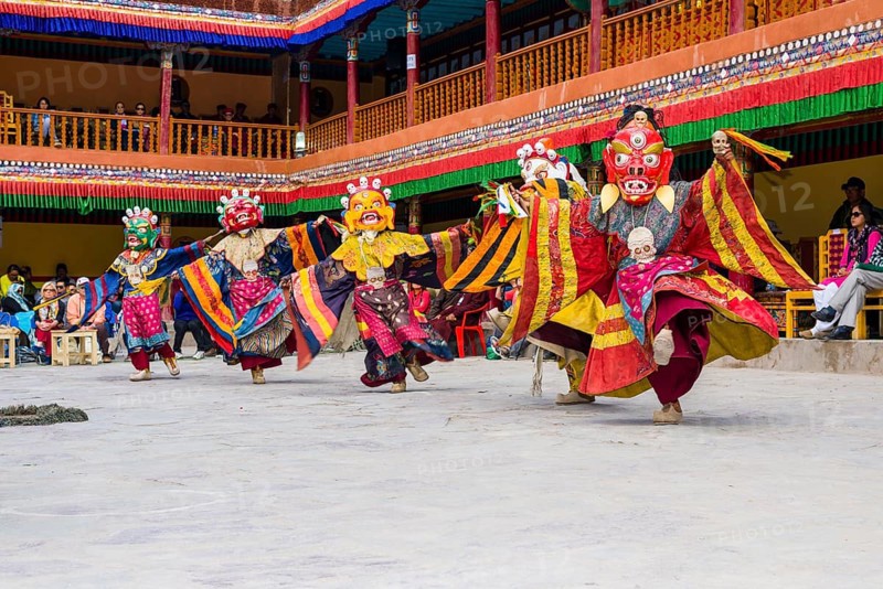 Monks with big wooden masks and colorful costumes are performing ritual dances at Hemis Festival in the courtyard of the monastery