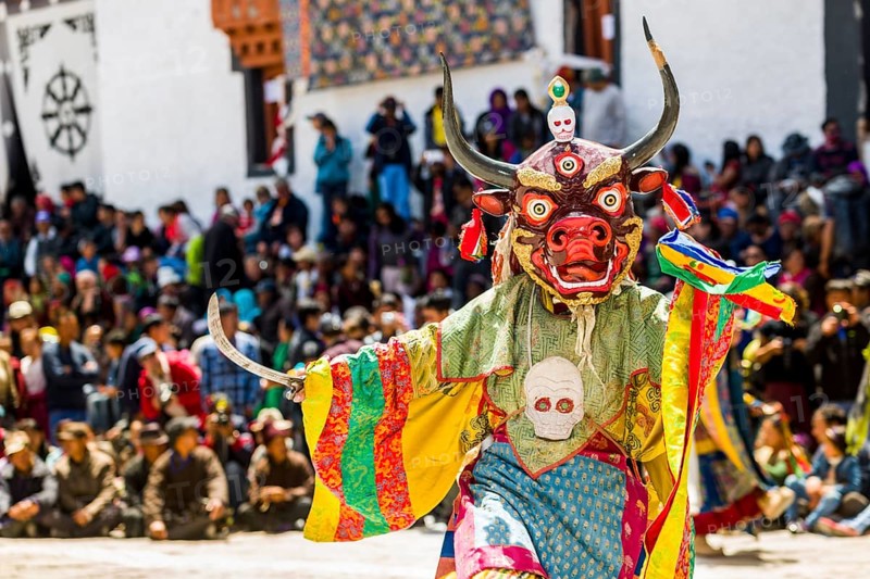 Monks with big wooden masks and colorful costumes are performing ritual dances at Hemis Festival in the courtyard of the monastery