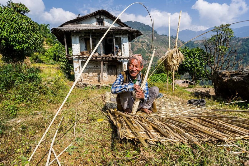 Man building a woven bamboo fence to be used as a wall in front of his farmers house