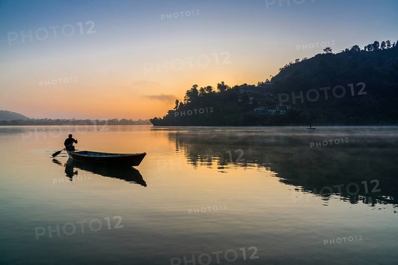 Man paddling a boat across Phewa Lake at sunrise