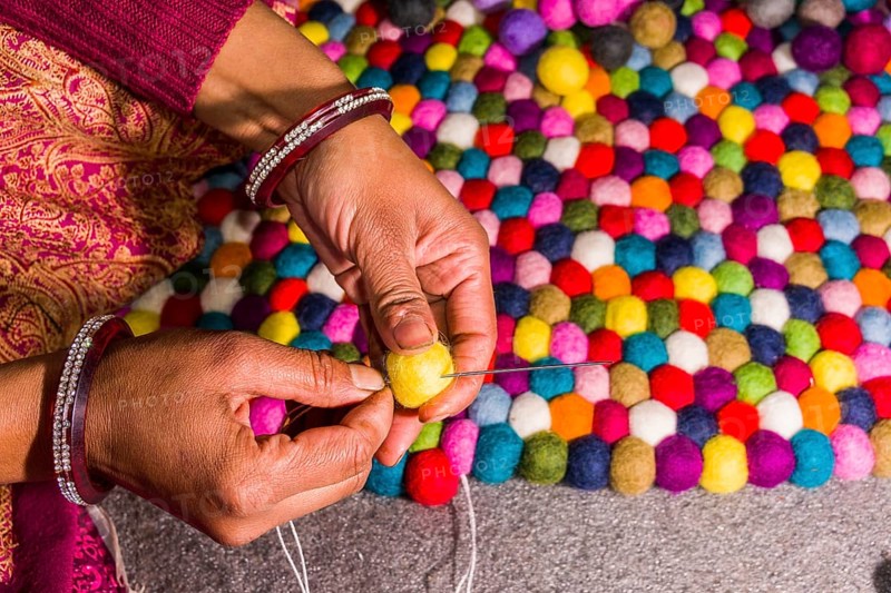 Hands of a woman are producing a carpet from felt balls