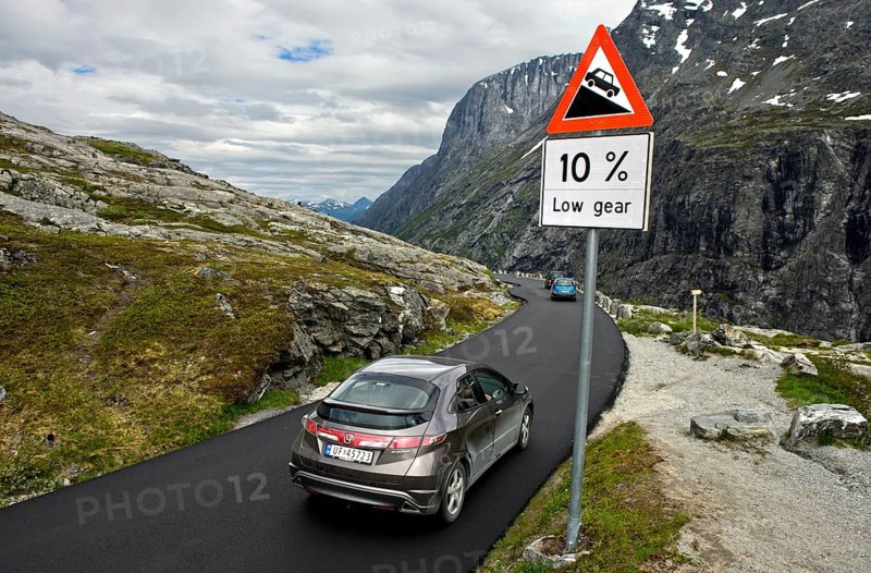 Cars by a warning sign in front of a steep slope