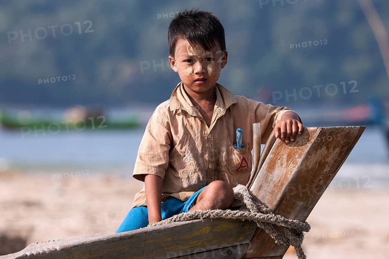 Local boy with Thanaka paste on his face sitting on the bow of a fishing boat