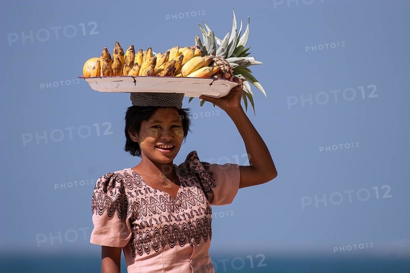 Native woman with a bowl of bananas on her head and Thanaka paste on her face