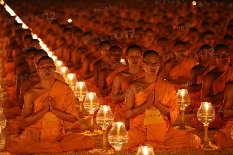 Monks sitting in rows praying and meditating by candlelight