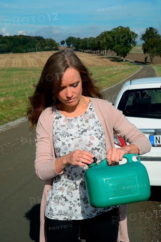 Young brunette woman holding a petrol can walking on a country road
