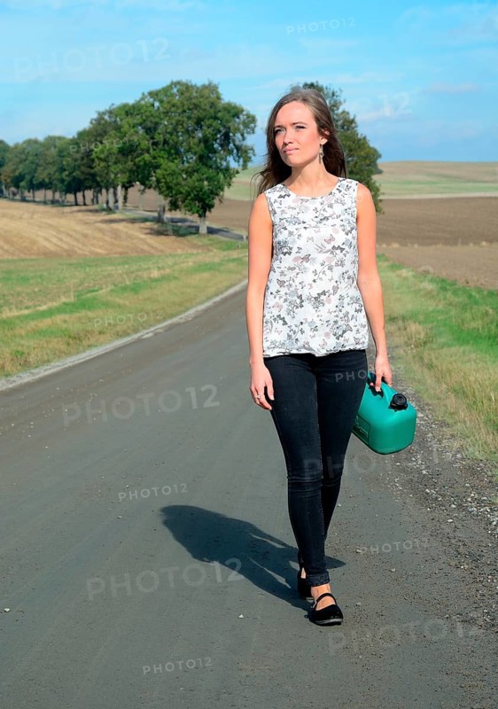 Young brunette with petrol can walking on country road