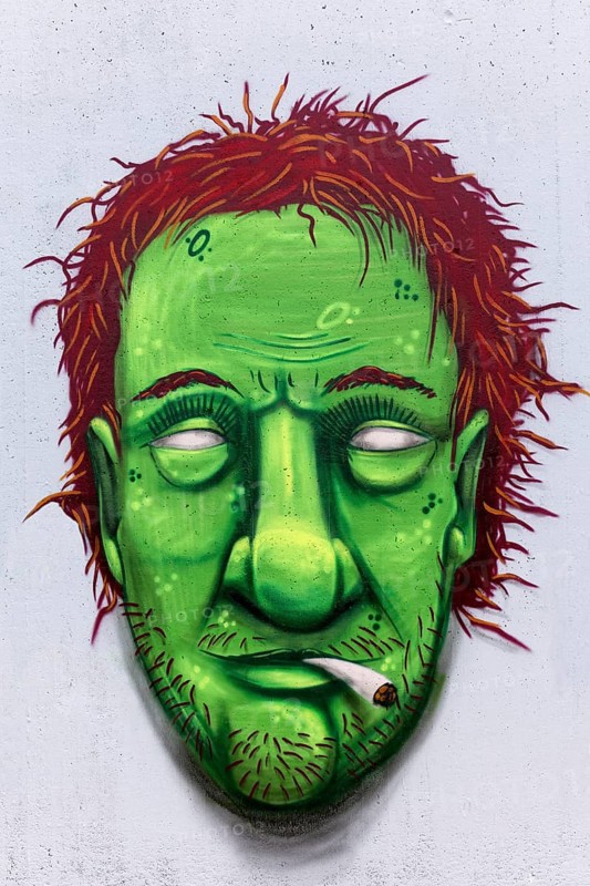 Portrait of a man with a green face smoking weed