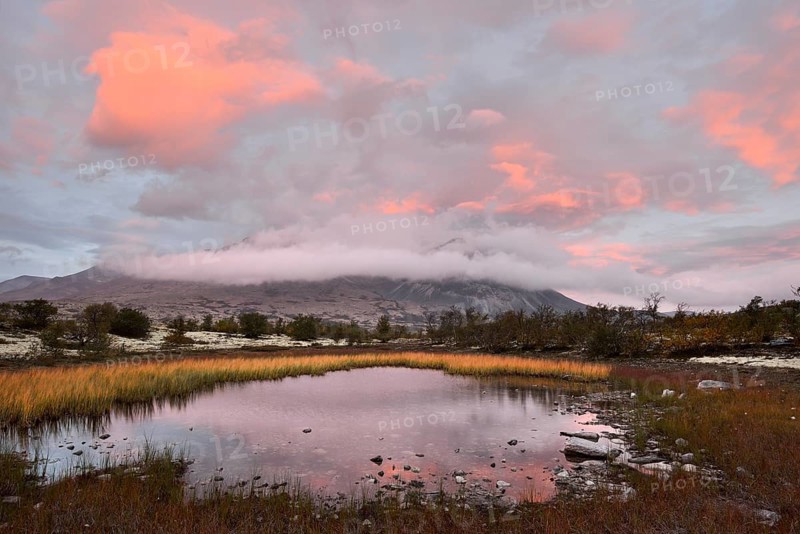 Red sky and mist in the morning above the peaks of the Stygghoin or Stygghoin mountain group reflected in a small lake