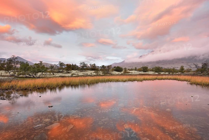 Red sky and mist in the morning above the peaks of the Stygghoin or Stygghoin mountain group reflected in a small lake