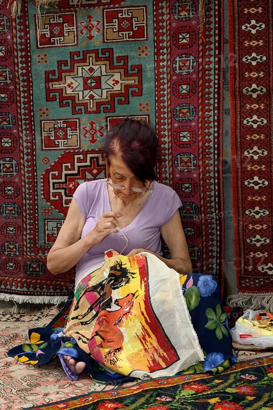 Woman doing embroidery in front of an Armenian carpet