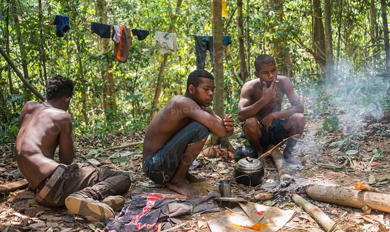 Three young aboriginal Orang Asil men sitting on the ground in the jungle