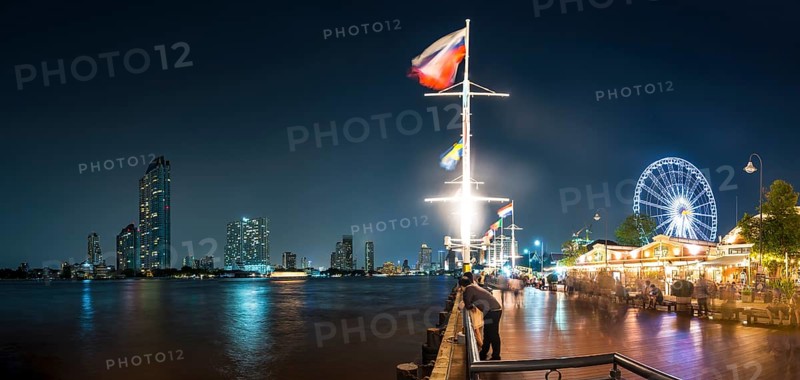 River promenade in the evening with a Ferris wheel and the skyline on the river Mae Nam Chao Phraya