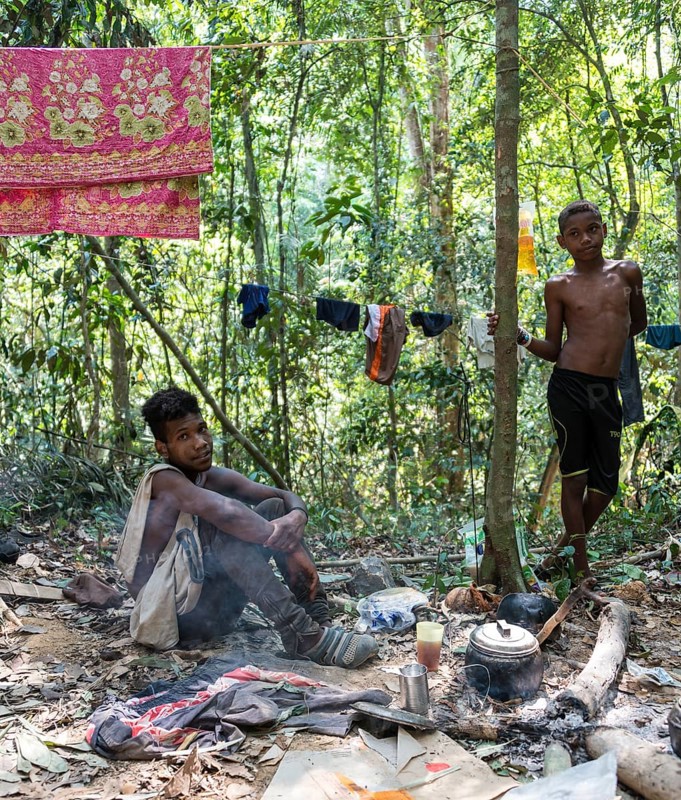 Two young men of the Orang Asil tribe sitting on the ground in the jungle and making tea