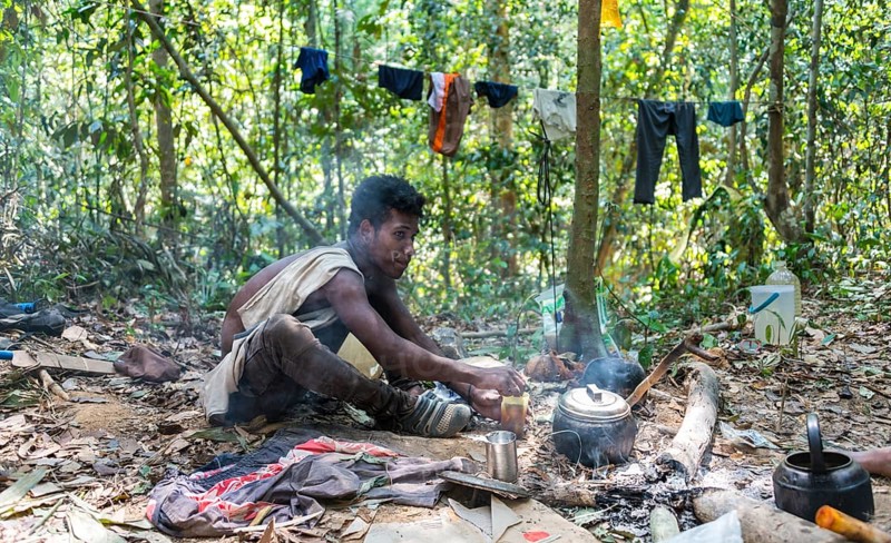 Young man of the Orang Asil tribe sitting on the floor in the jungle and making tea