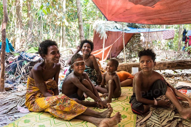 Women and children of the Orang Asil tribe sitting under tarpaulins in the jungle