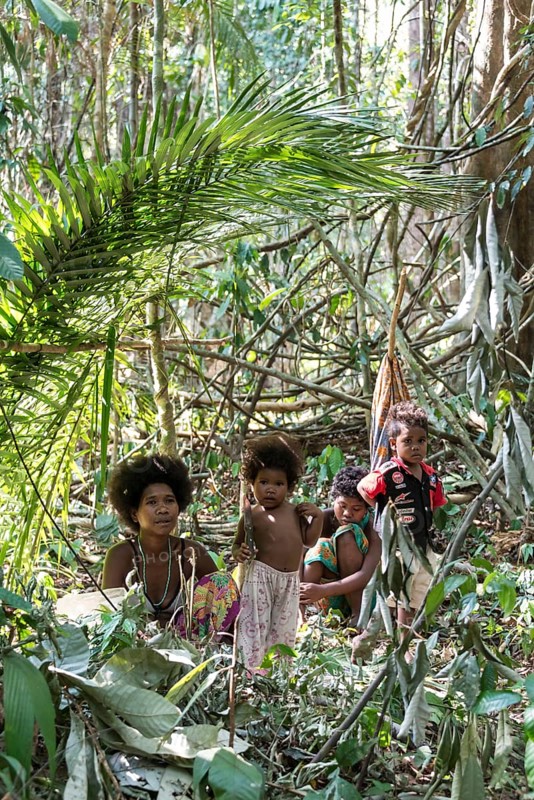 Woman of the Orang Asil tribe sitting with children under palm fronds in the jungle
