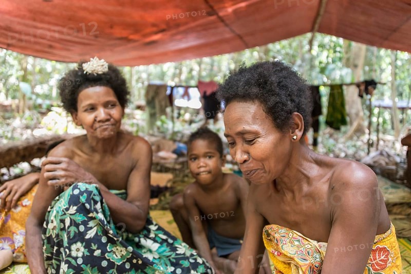 Women and children of the Orang Asil tribe sitting under tarpaulins in the jungle