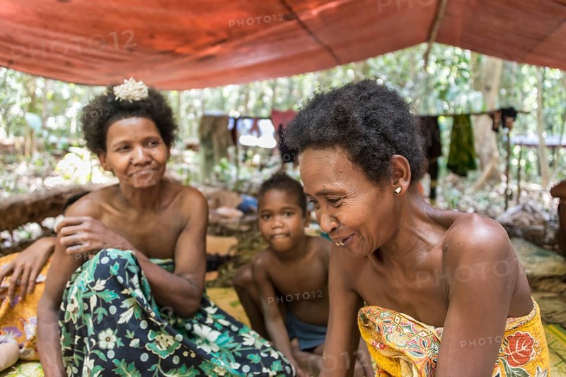 Women and children of the Orang Asil tribe sitting under tarpaulins in the jungle