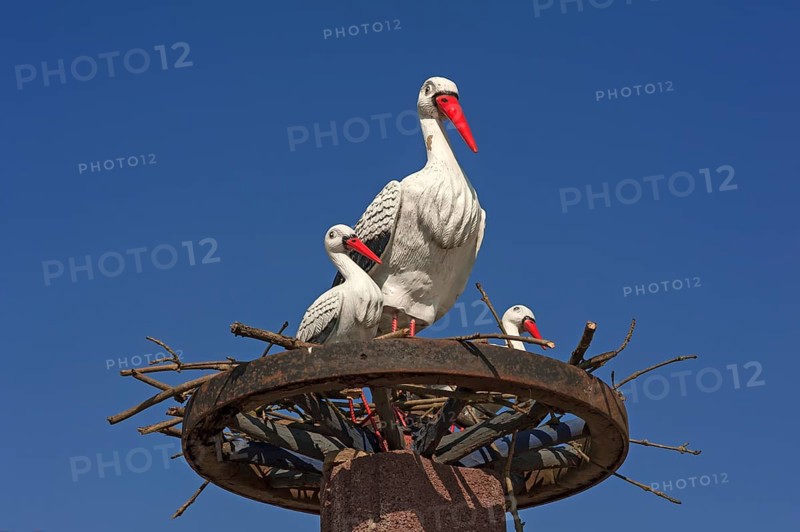Stork figures on a wagon wheel against blue sky
