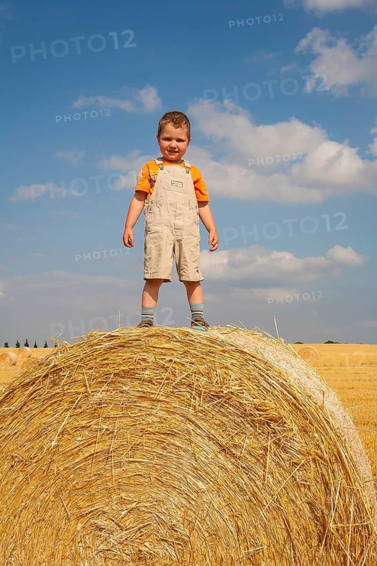 Little boy standing proudly on a straw bale