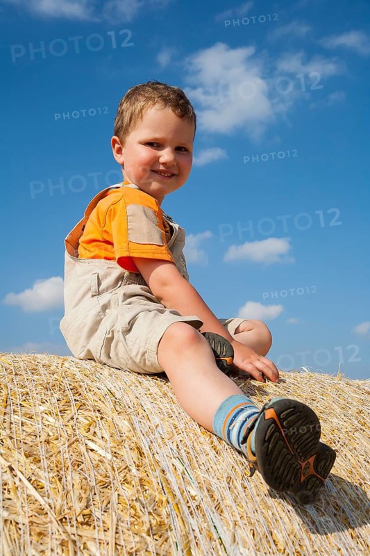 Little boy sitting on a straw bale under a cloudy blue sky