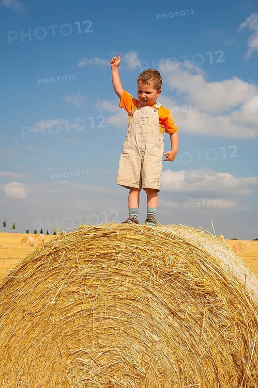 Little boy standing proudly on a straw bale