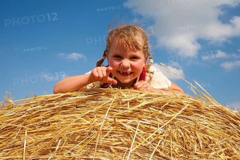 Little girl lying on a straw bale under a cloudy blue sky