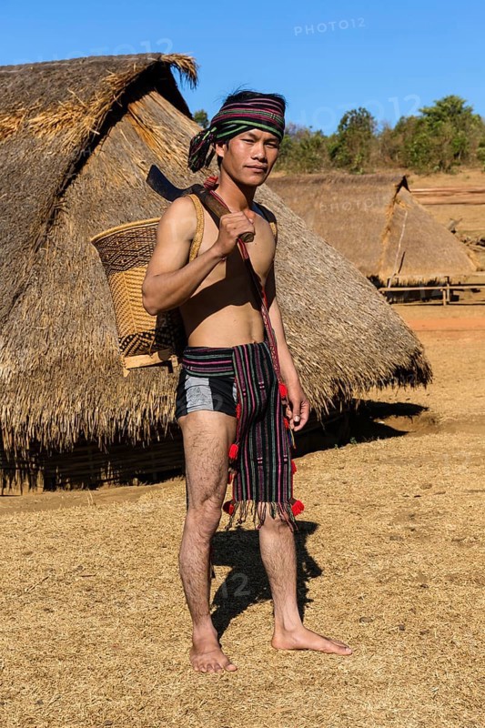 Man in traditional costume in front of a Phnong house