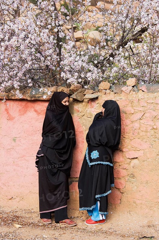 Berber women chatting in front of a wall with blossoming almond trees