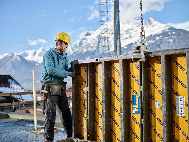 Construction worker lifting shuttering wall with crane