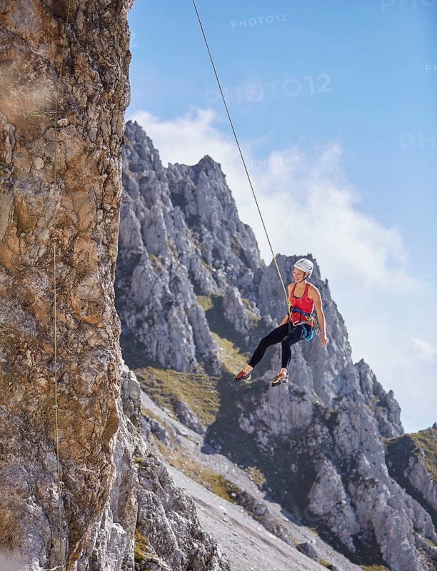 Climber with helmet swinging on climbing rope on rock face