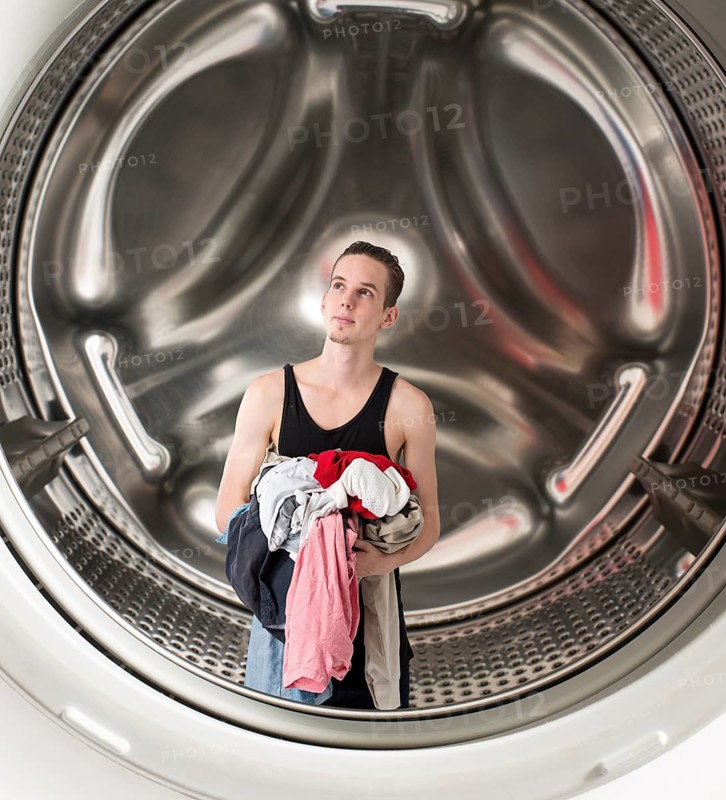 Conceptual image of a young confused man holding laundry inside a washing machine