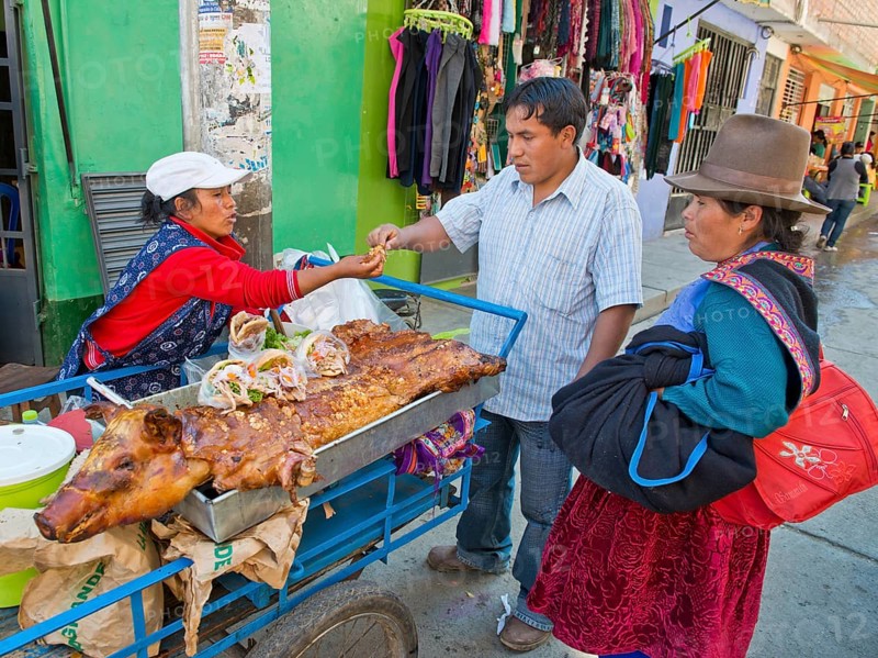 A Quechua Indian woman selling roasted suckling pig and sandwiches on the road