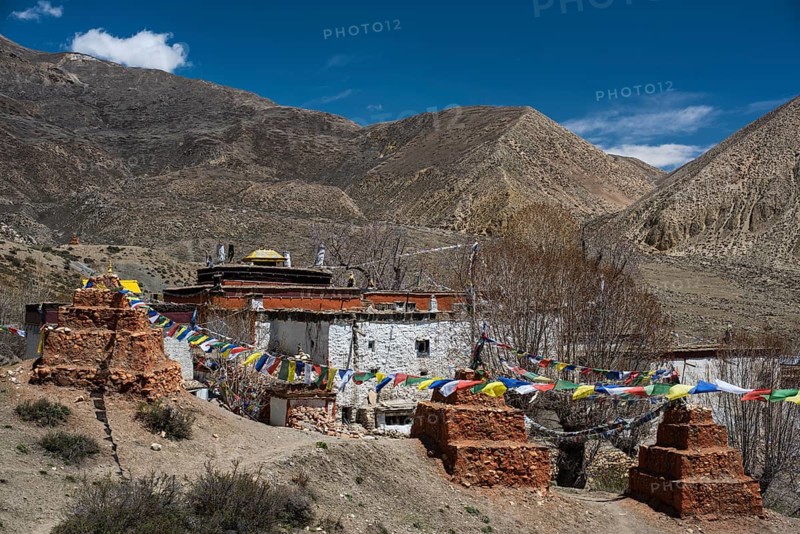Ghar Gompa of Lo Gekar with prayer flags in front of mountain landscape