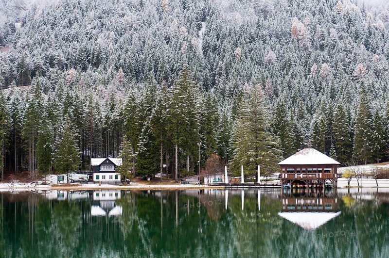 Snow-covered forest and houses reflected in Lake Toblach