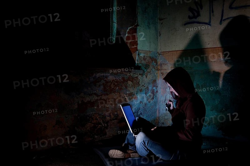 Female computer hacker sitting with a laptop in the dark