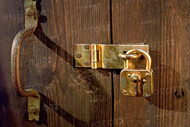 Old wooden door locked with metal fittings and a padlock