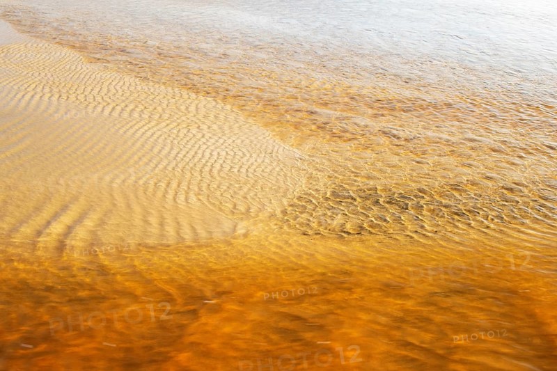 Reddish ferruginous water flows over a sandy beach at low tide