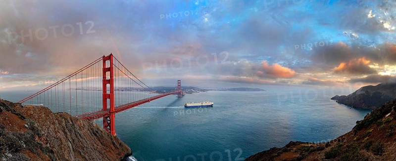 Panoramic view of the Golden Gate Bridge at sunset with a rainbow and storm clouds