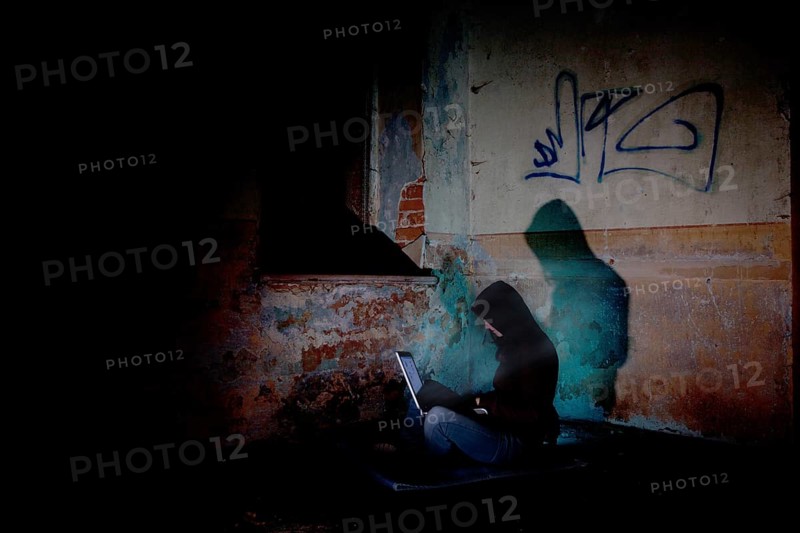 Female computer hacker sitting with a laptop in the dark