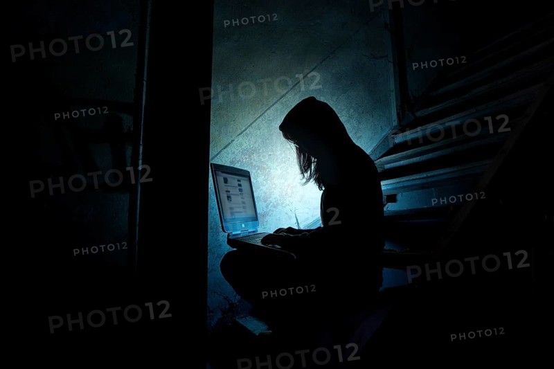 Female computer hacker sitting with a laptop in the dark