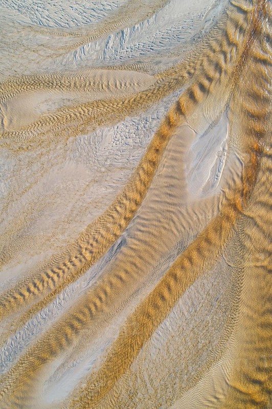 Creek with reddish ferruginous water flows over a sandy beach into the sea