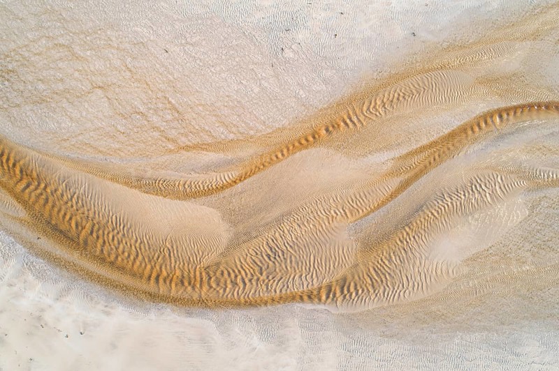 Creek with reddish ferruginous water flows over a sandy beach into the sea