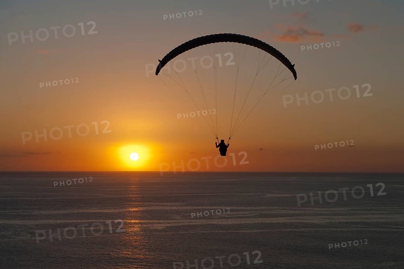 Paraglider over the Atlantic Ocean with sunset